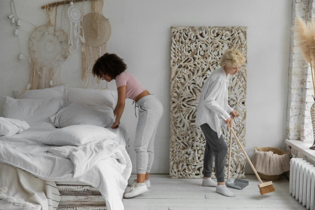 Professional cleaners making a bed and sweeping in a bright residential bedroom